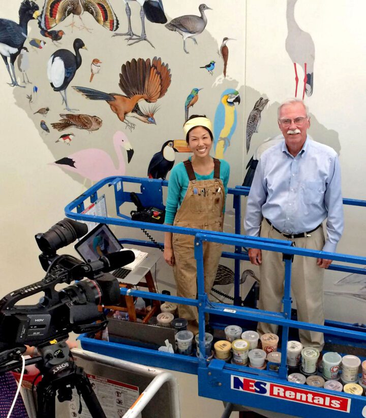 two people in a lift in front of a mural.