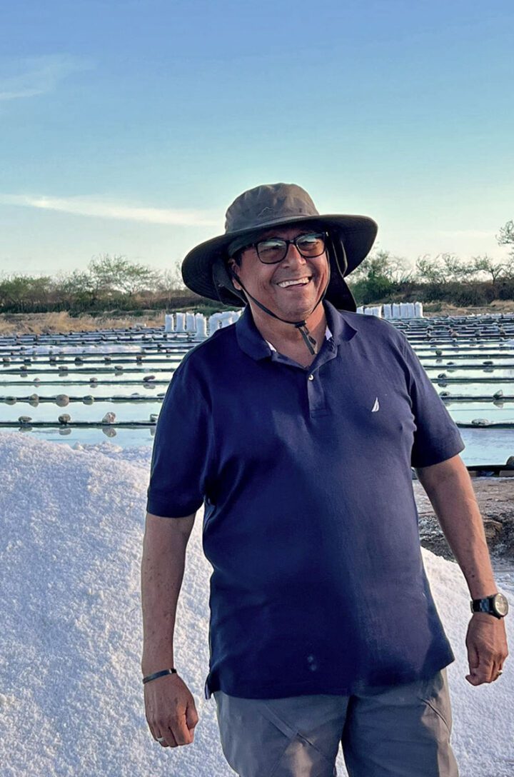 Man in a blue shirt and hat stands in front of a giant pile of salt.